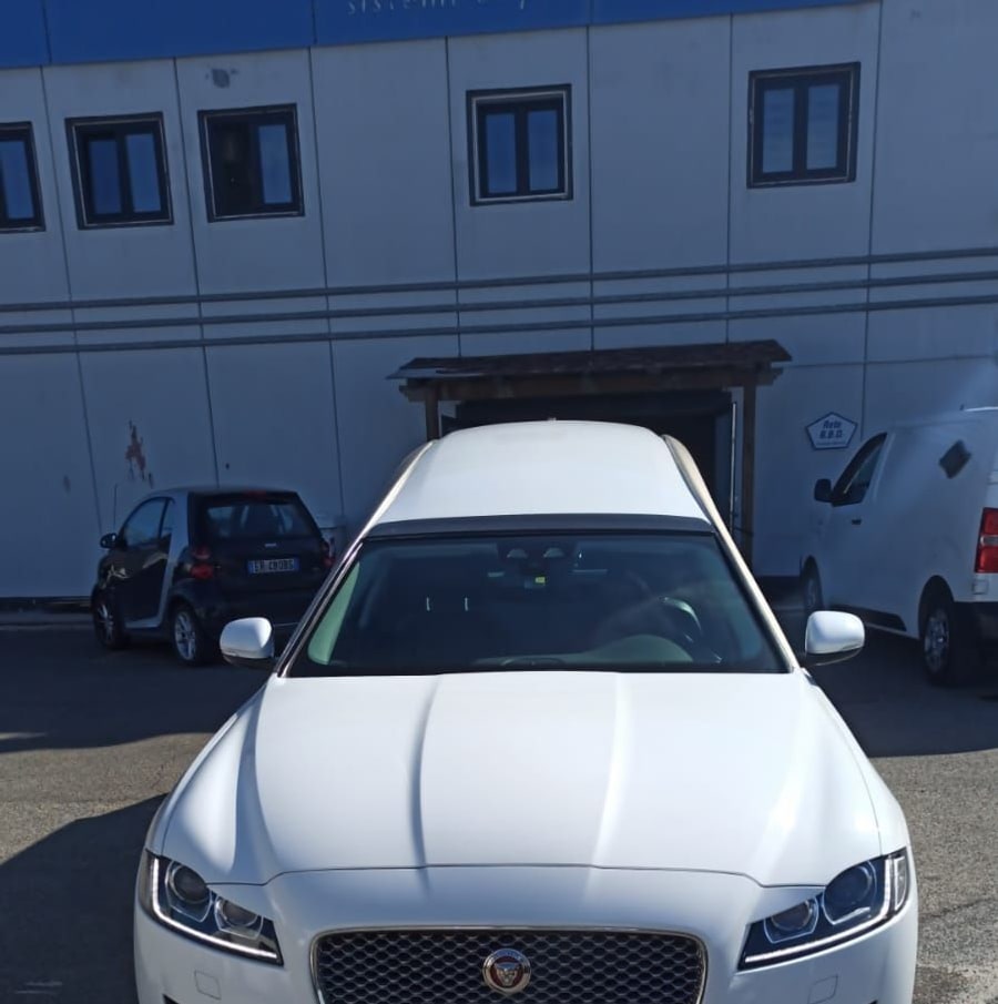 Il frontale di un carro funebre Jaguar bianco, davanti alla rimessa