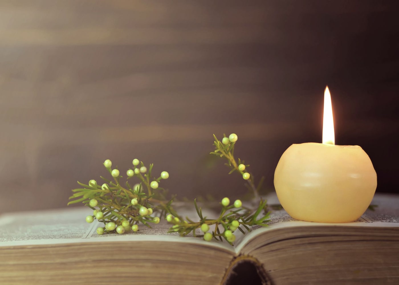 Un cero acceso accanto a un libro aperto e a un rametto verde