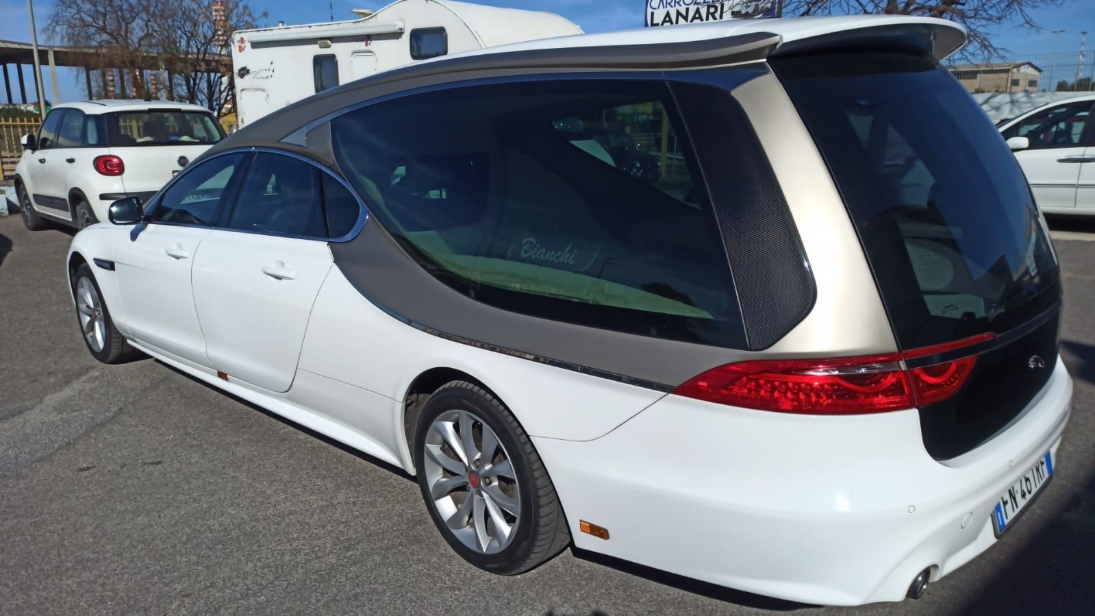 Un carro funebre bianco visto di fianco, davanti alla rimessa